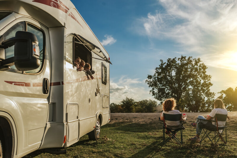 Children leaning out of the window of the caravan, watching their mothers drinking coffee. Concept of family in caravan