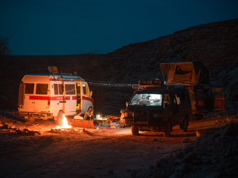Buscamper in het donker met voor de camper een vuurtje
