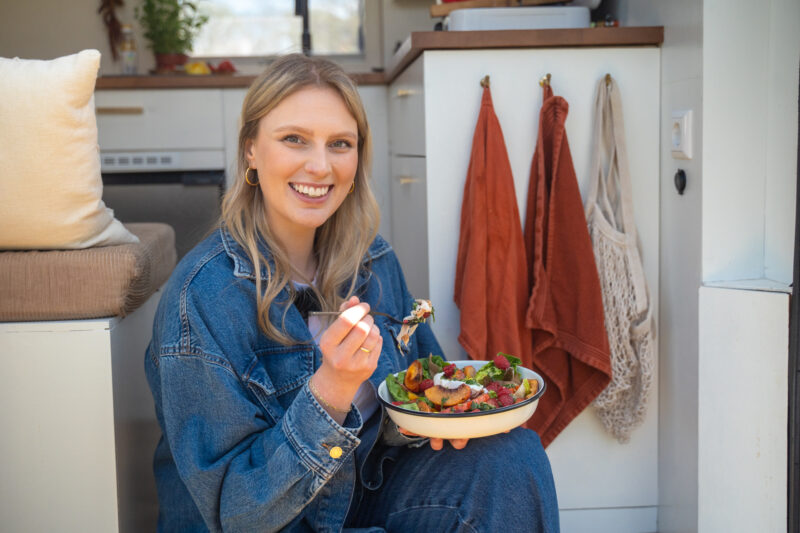 Marieke Plant in de deuropening van de camper met op haar schoot een salade burrata