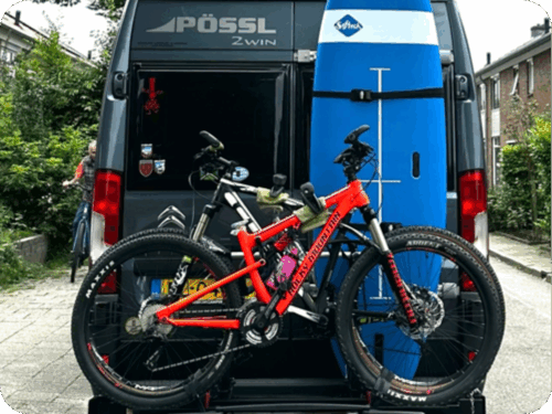 Camperbus met fiets en surfplank achterop - ter illustratie