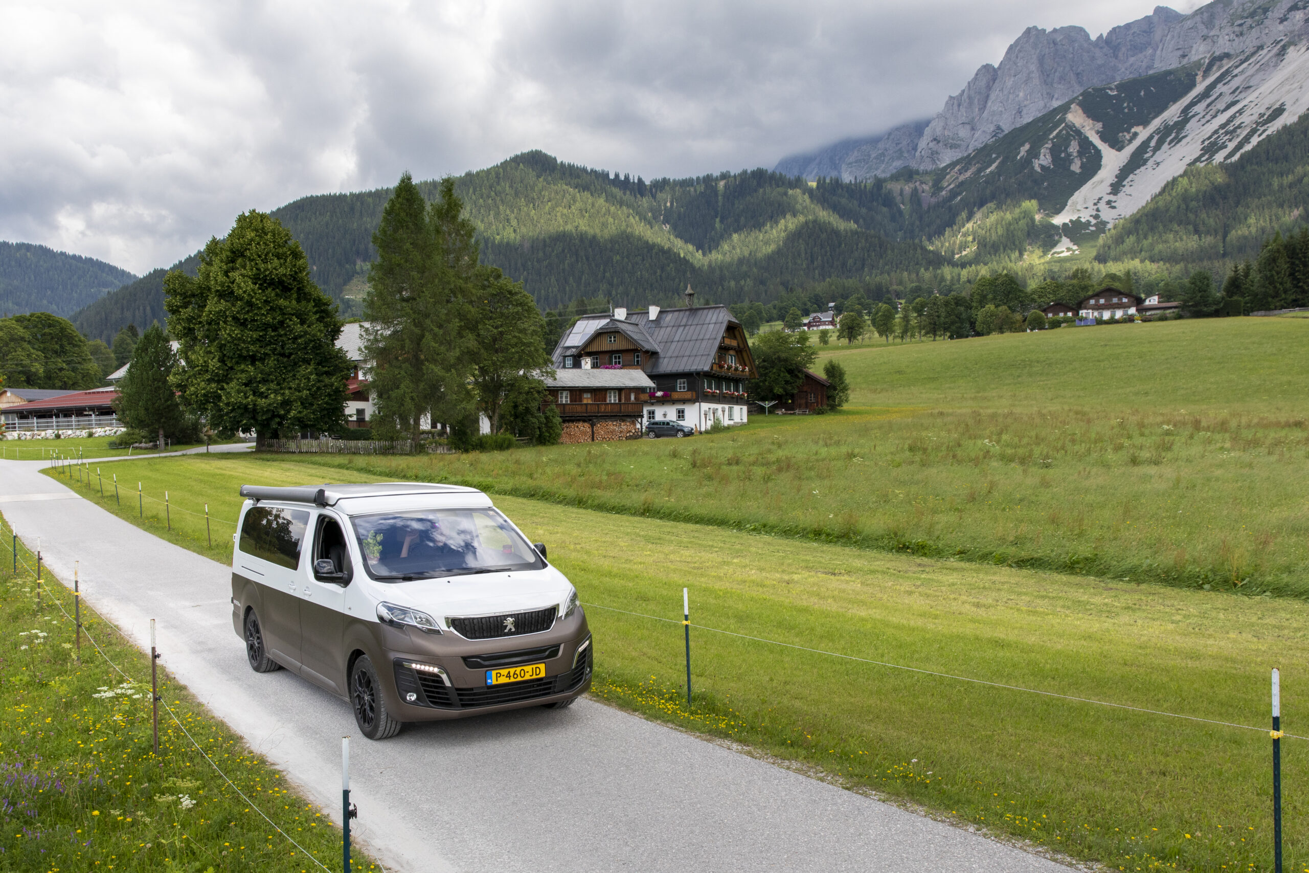 elektrische camper op een weg tussen groene weilanden in de alpen