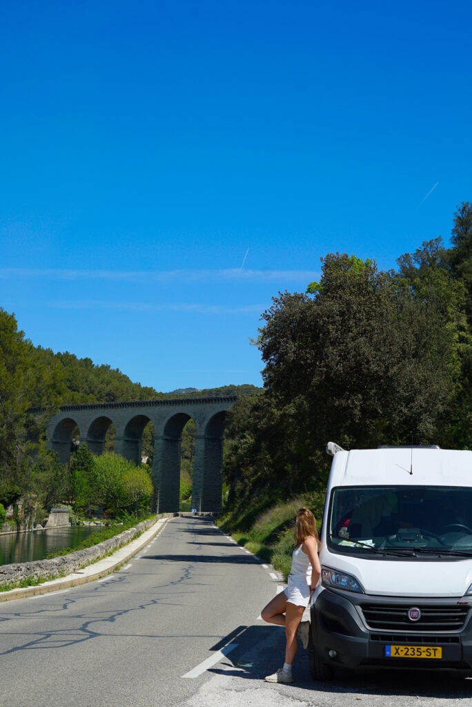 camper met vrouw en Romeinse brug op de achtergrond